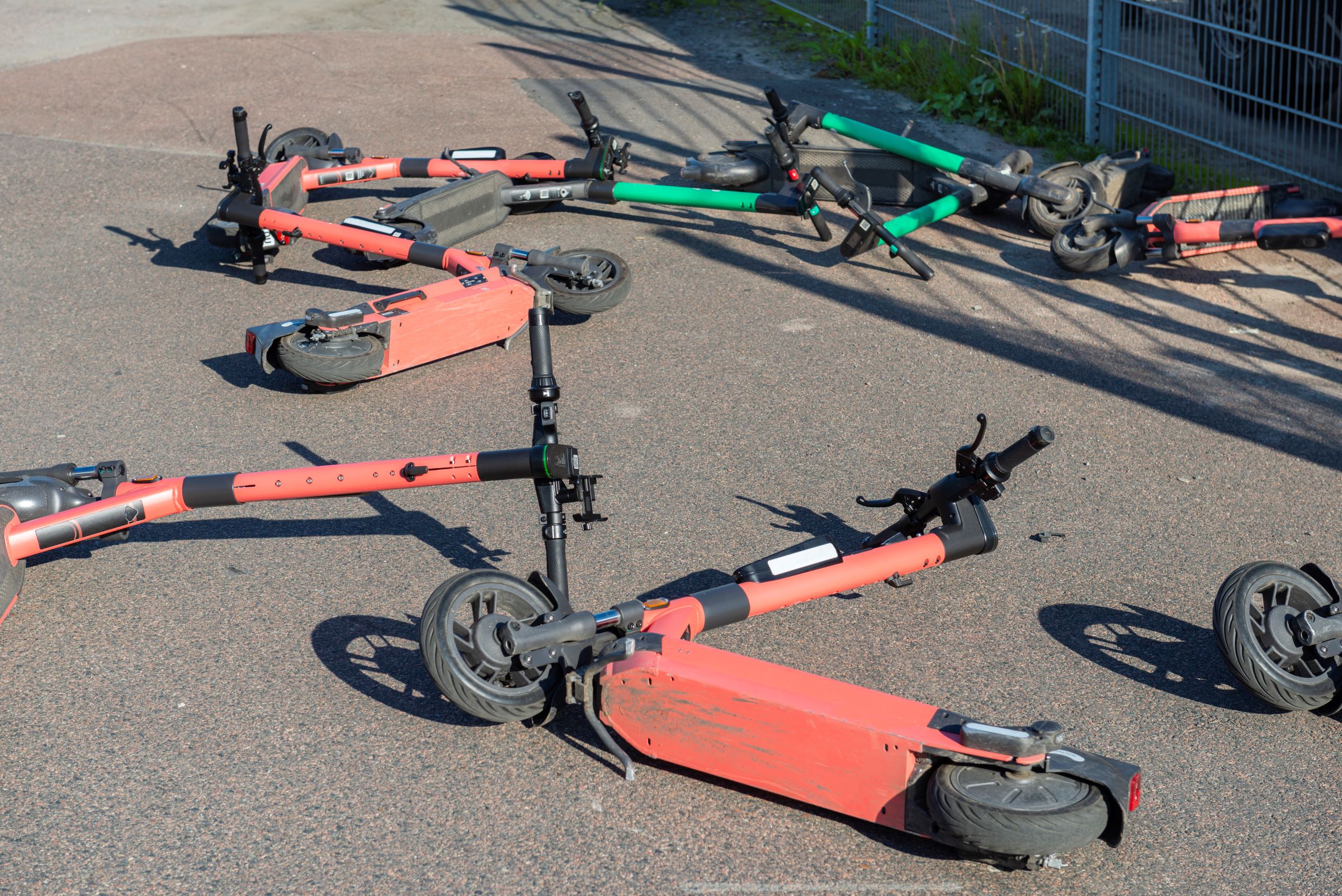 Der Betrachter steht auf einem Asphaltweg und vor ihm liegen kreuz und quer 8 E-Scooter auf dem Boden.